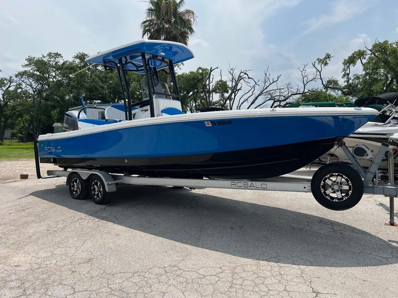 The Image of 2018 Robalo 246 Cayman boat on trailer, blue and black design, parked outdoors. - 0