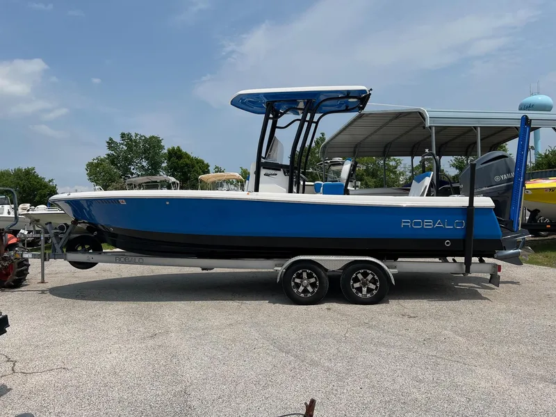 Slide: The Image of 2018 Robalo 246 Cayman boat on trailer, blue and white, parked outdoors. - 1