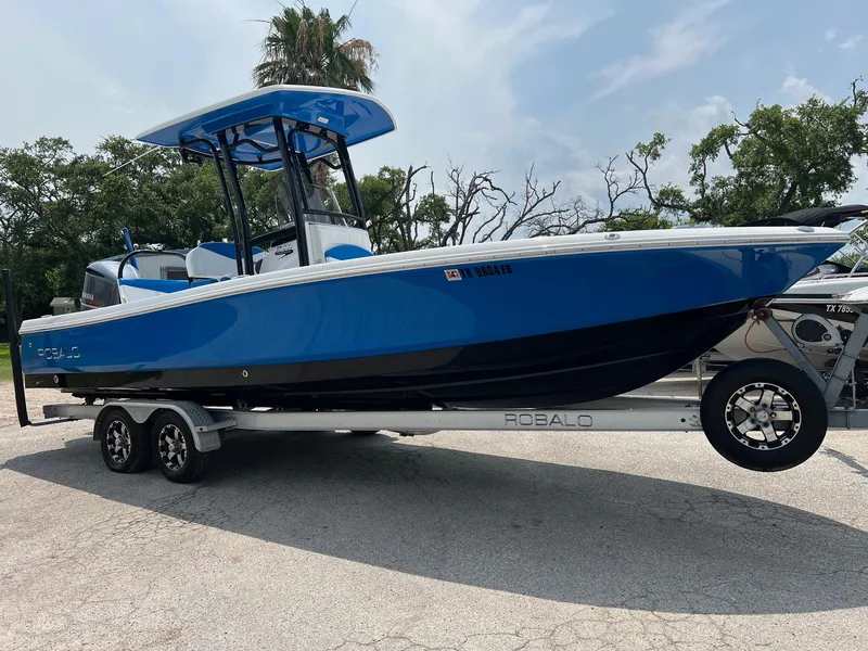 Slide: The Image of 2018 Robalo 246 Cayman boat on trailer, blue and white design, parked outdoors. - 8