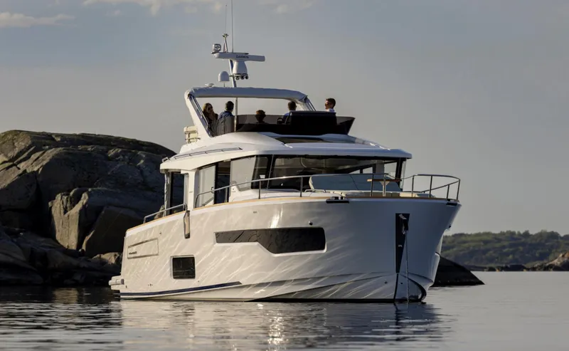 Slide: The Image of 2025 Nimbus 495 Flybridge yacht on calm water near rocky shoreline. - 30