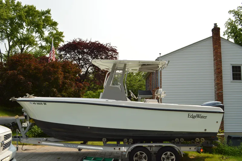 Slide: The Image of 2007 Edgewater 228CC boat on trailer, parked beside a house with trees in the background. - 4