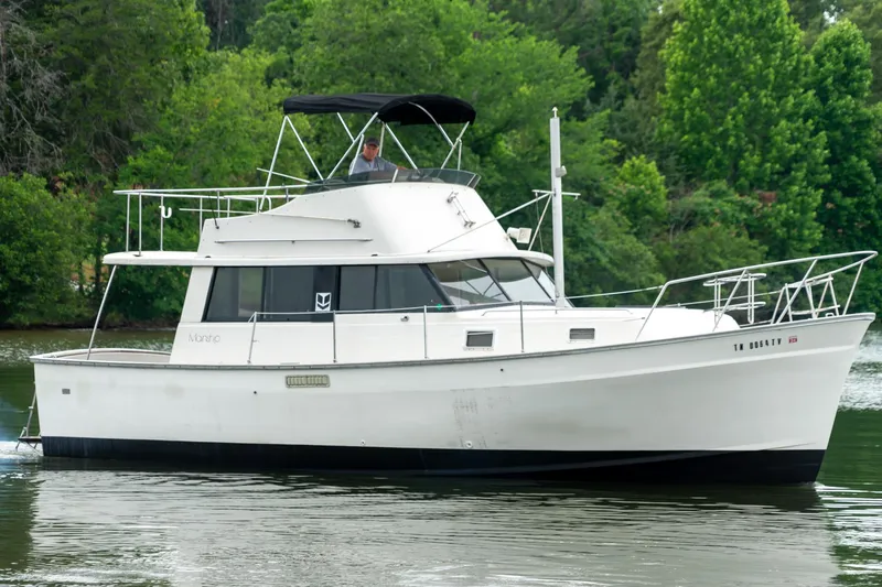 Slide: The Image of 1979 Mainship 34 boat cruising on a calm river with lush green trees in the background. - 2