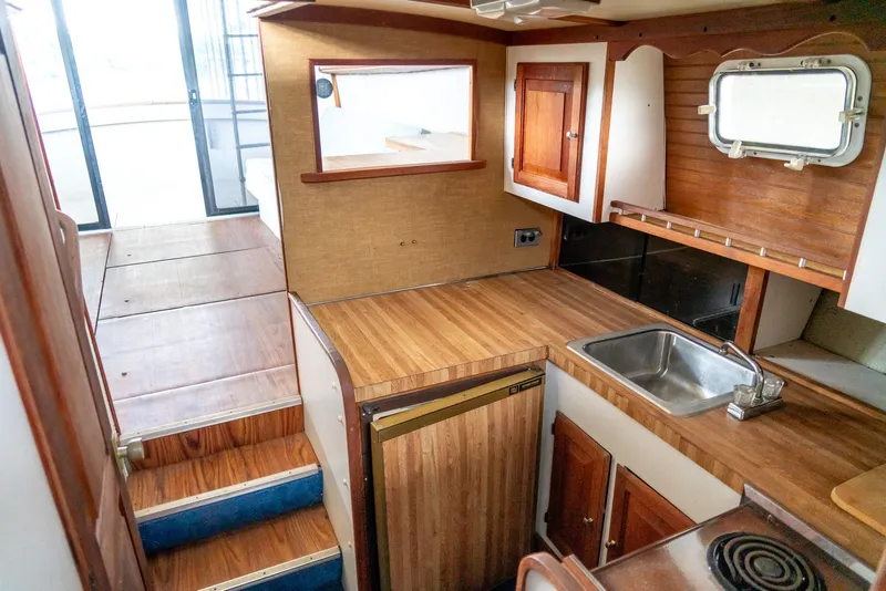Slide: The Image of 1979 Mainship 34 boat interior with wooden cabinetry, compact kitchen, and stairs leading to deck. - 24