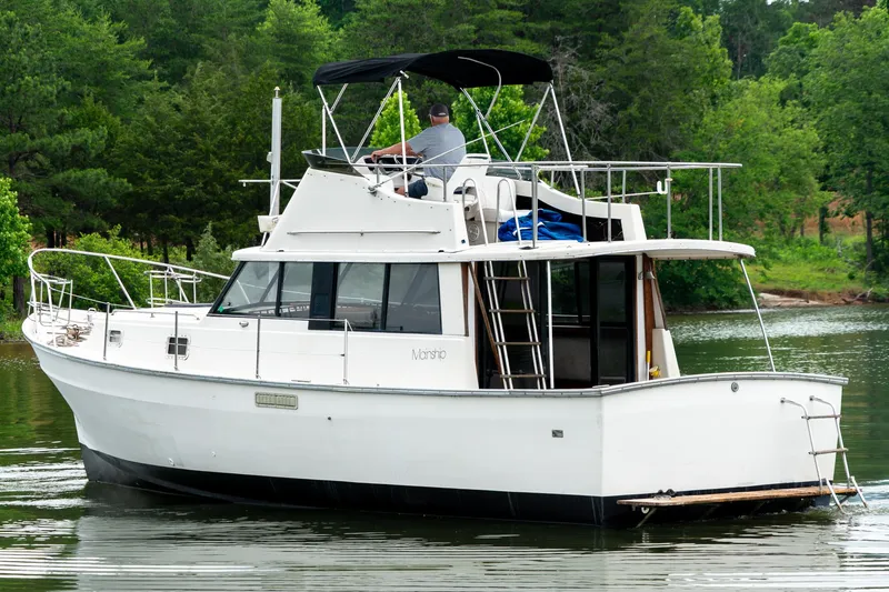 Slide: The Image of 1979 Mainship 34 boat cruising on a serene lake with lush green trees. - 4