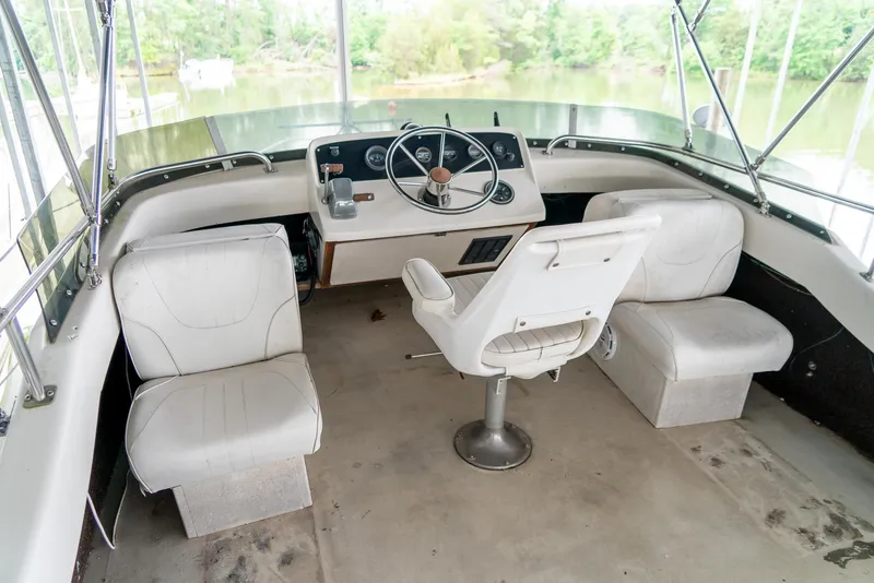 Slide: The Image of 1979 Mainship 34 boat helm with white seating and steering wheel, overlooking a serene water view. - 9