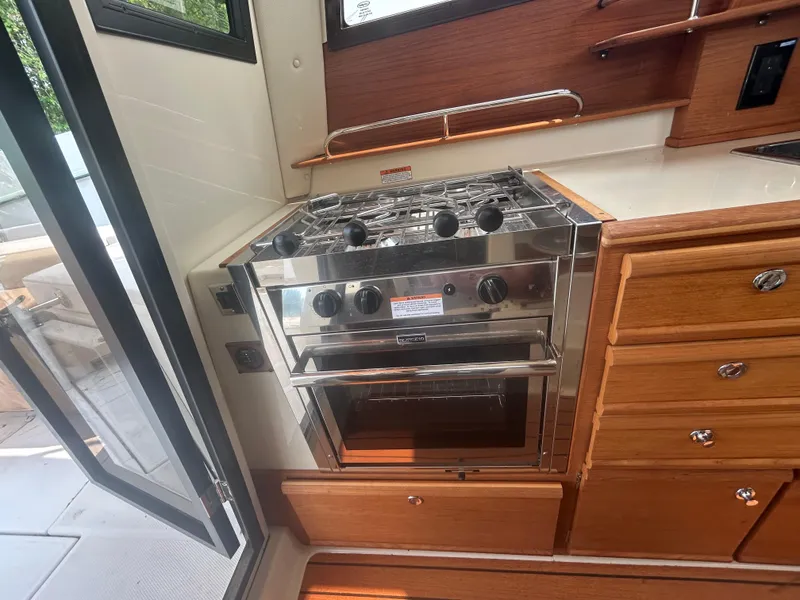 Slide: The Image of 2021 Ranger Tugs R-27 boat kitchen with stainless steel stove and wooden cabinetry. - 12