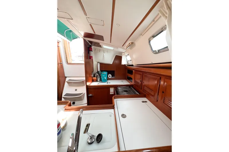 Slide: The Image of Interior of 2002 Beneteau 361 sailboat, featuring a compact kitchen with wooden cabinetry. - 14