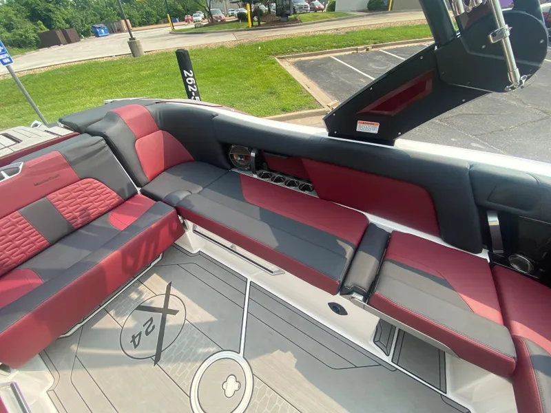 Slide: The Image of 2022 MasterCraft X24 boat interior with red and gray seating, docked in a parking area. - 17
