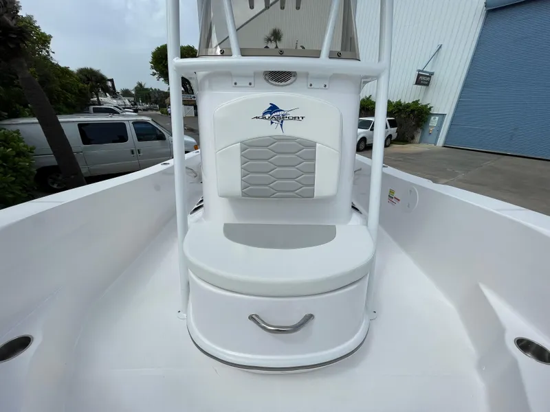 Slide: The Image of 2024 Aquasport 230 Pro Bay boat interior with seating and storage, docked near a warehouse. - 8
