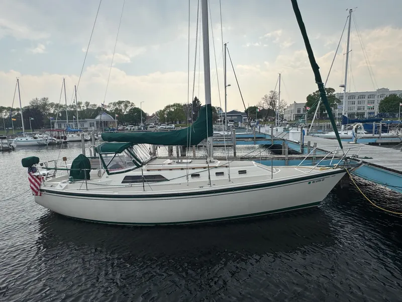Slide: The Image of 1984 O'Day 34 Sloop sailboat docked at a marina, featuring green sail covers. - 1