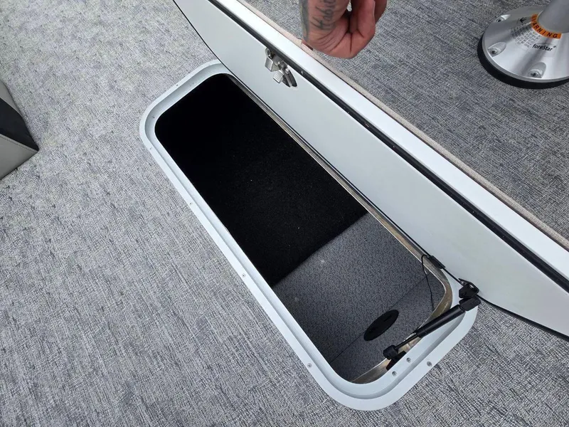 Slide: The Image of 2025 Berkshire 22 RFX LE boat storage compartment with open hatch on gray carpeted floor. - 19