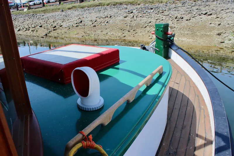 Slide: The Image of 1961 Custom 32' William Garden Tugboat with green deck and red cushion, docked by rocky shore. - 6