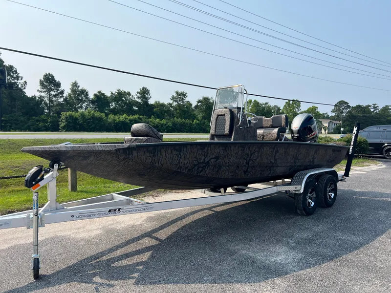 Slide: The Image of 2025 Xpress H20B boat on trailer, parked outdoors, with trees in the background. - 2