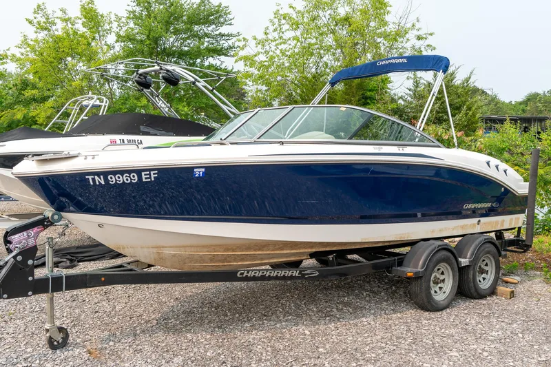 Slide: The Image of 2014 Chaparral 21 Ski & Fish H2O boat on trailer, blue and white design, parked outdoors. - 4