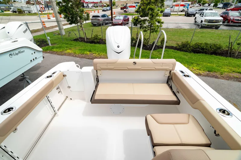 Slide: The Image of 2026 Edgewater 248 CX boat interior with beige seating and motor, parked outdoors. - 11