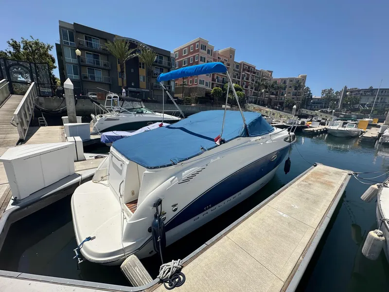 Slide: The Image of 2008 Bayliner 265 boat docked at marina with blue cover and nearby buildings. - 4