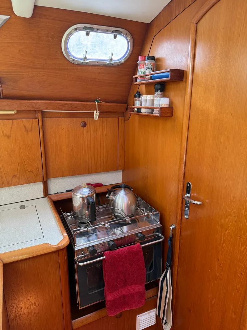 Slide: The Image of Jeanneau Sun Odyssey 36.2 yacht kitchen with stove, wooden cabinets, and porthole window, year 2000. - 16