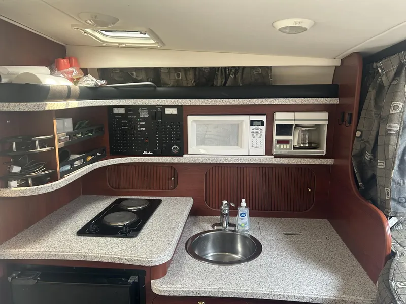 Slide: The Image of 2002 Rinker 342 Fiesta Vee boat kitchen with stove, sink, microwave, and storage shelves. - 12