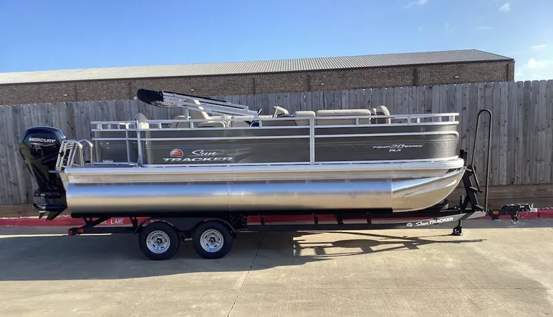 The Image of 2025 Sun Tracker Fishin' Barge 20 DLX pontoon boat on trailer, parked outdoors. - 0