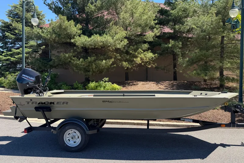 Slide: The Image of 2025 Tracker Grizzly 1654 T Sportsman boat on trailer, parked outdoors near trees. - 4
