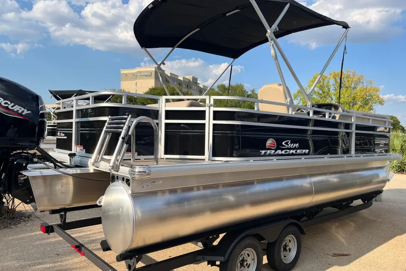 Slide: The Image of 2025 Sun Tracker SportFish 22 DLX pontoon boat on trailer, under blue sky. - 2