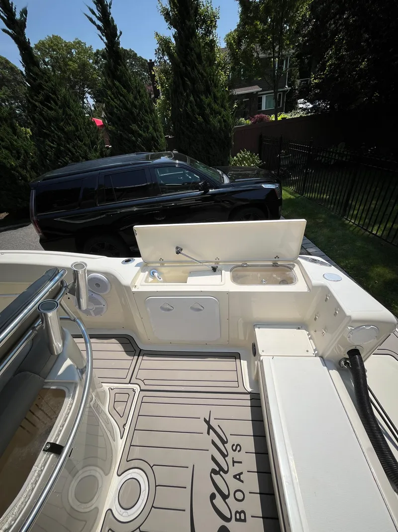 Slide: The Image of 2023 Scout 235 Sportfish boat with open storage, parked near a black vehicle. - 17