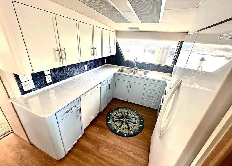 Slide: The Image of 1994 Hatteras Cockpit Motoryacht kitchen with white cabinets, marble countertops, and nautical-themed floor mat. - 12