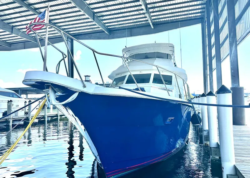 Slide: The Image of 1994 Hatteras Cockpit Motoryacht docked under a covered marina with American flag. - 34