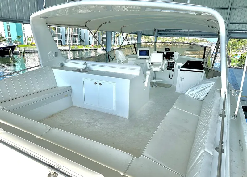 Slide: The Image of 1994 Hatteras Cockpit Motoryacht interior with seating, helm, and kitchenette under a covered dock. - 6