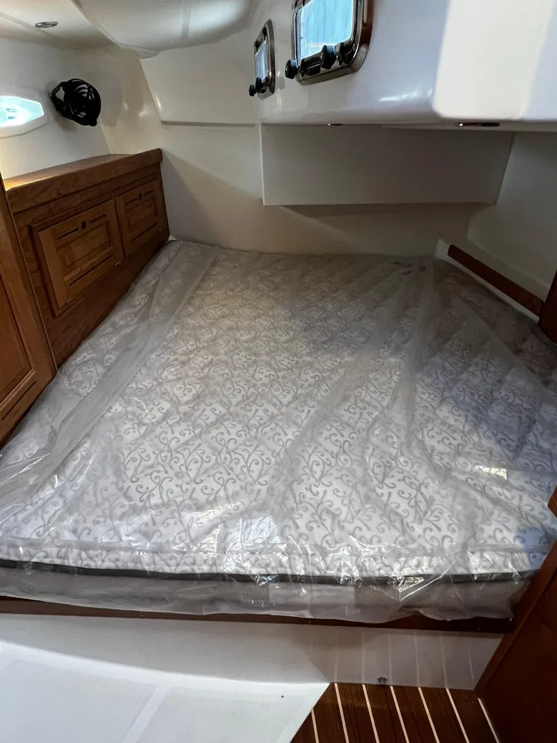 Slide: The Image of 2025 Tartan 395 cabin interior with bed, wooden cabinetry, and portholes. - 24