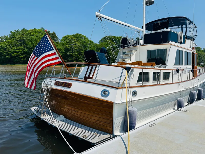 Slide: The Image of 1998 Grand Banks 49 Classic yacht docked, displaying American flag, surrounded by lush greenery. - 6