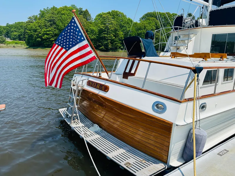 Slide: The Image of 1998 Grand Banks 49 Classic yacht with American flag, docked by lush greenery. - 7