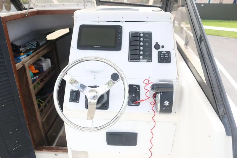 Slide: The Image of 1990 Mako 230 Walk Around boat dashboard with steering wheel and control panel. - 19