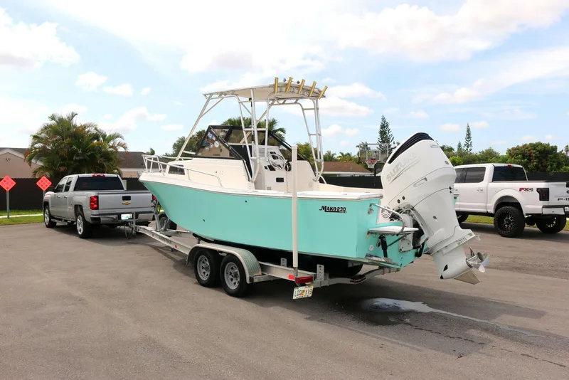 Slide: The Image of 1990 Mako 230 Walk Around boat on trailer, parked near pickup trucks, under a partly cloudy sky. - 21