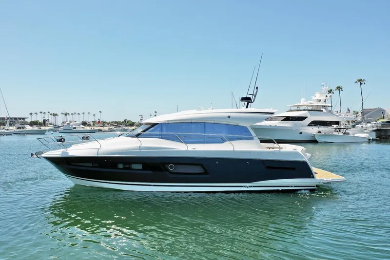 Slide: The Image of 2020 Prestige 460S yacht on calm water, with marina and palm trees in background. - 2
