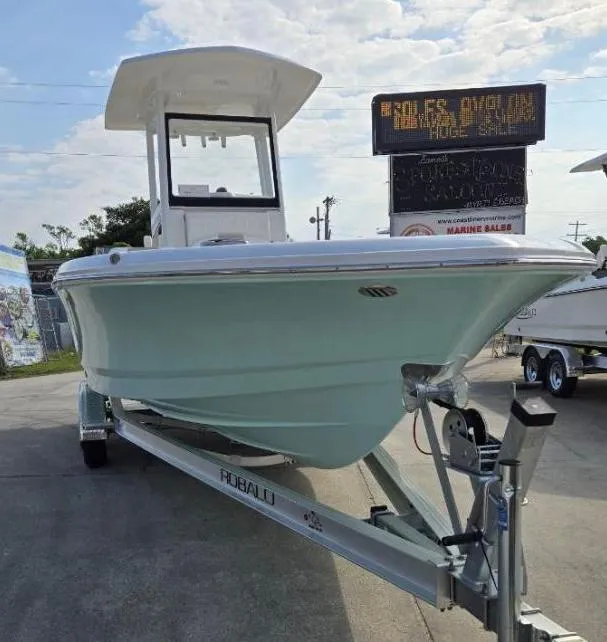 Slide: The Image of 2024 Robalo 246 Cayman boat on trailer, displayed outdoors under a partly cloudy sky. - 2