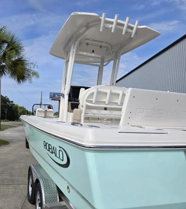 Slide: The Image of 2024 Robalo 246 Cayman boat on trailer, light blue hull, palm tree in background. - 7