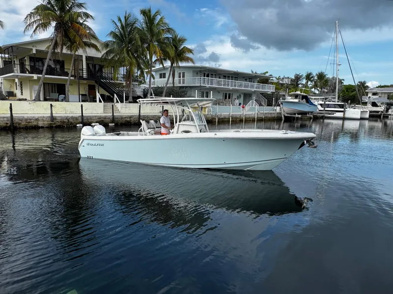 The Image of 2022 Sailfish 290 CC boat docked in a marina with palm trees and buildings. - 0