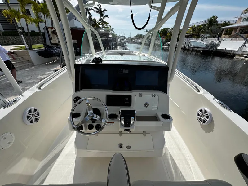 Slide: The Image of 2022 Sailfish 290 CC boat cockpit with steering wheel and dual screens, docked by a canal. - 19