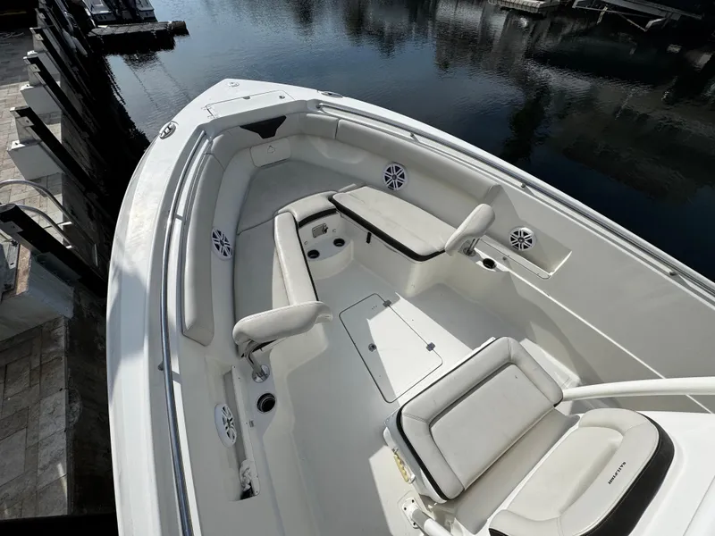 Slide: The Image of 2022 Sailfish 290 CC boat interior with white seating and speakers, docked by calm water. - 5