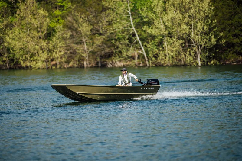 Slide: The Image of 2025 Lowe L1448M Jon boat cruising on a scenic lake with lush green trees. - 5