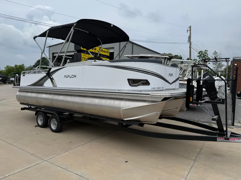 Slide: The Image of 2025 Avalon LSZ Versatile Rear Lounger pontoon boat on trailer, parked outdoors. - 1