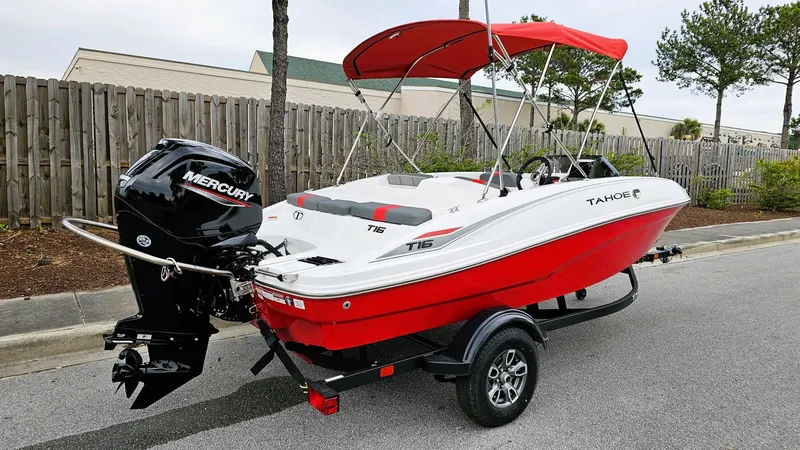 Slide: The Image of 2025 Tahoe T16 boat with Mercury engine, red and white design, parked on trailer. - 1