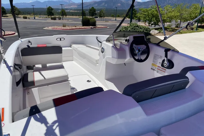 Slide: The Image of 2025 Tahoe T16 boat interior with seating and steering wheel, parked outdoors with scenic mountain view. - 2