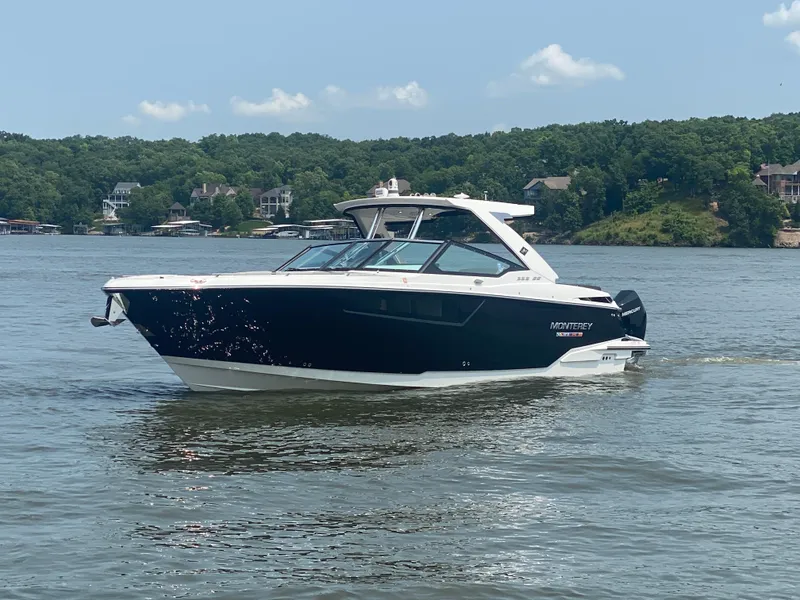 Slide: The Image of 2022 Monterey 385 Super Sport boat cruising on a serene lake with lush green shoreline. - 1