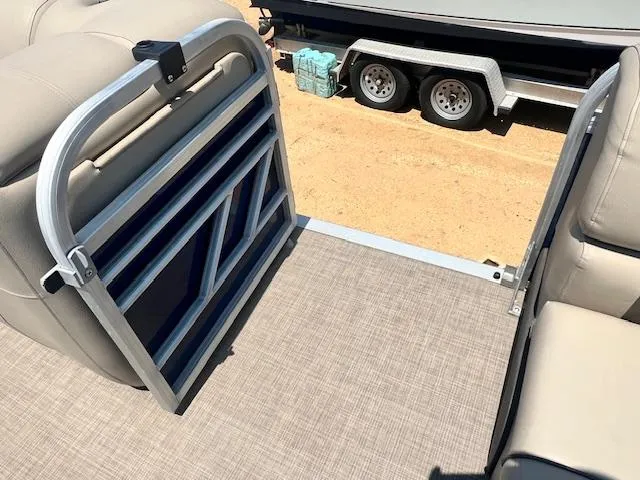 Slide: The Image of 2021 Sun Tracker Party Barge 20 DLX interior with gate and seating, parked on sandy ground. - 8