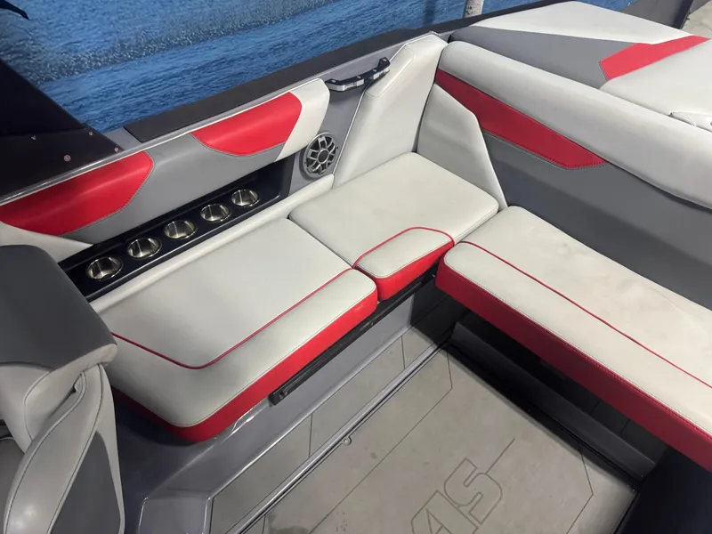 Slide: The Image of 2021 Axis A22 boat interior with red and white seating, cup holders, and speaker by the water. - 8