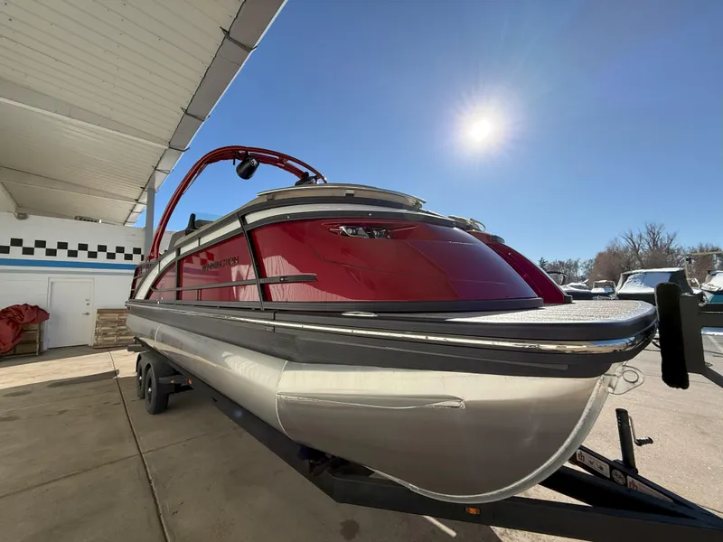 Slide: The Image of 2025 Bennington 25QXFB pontoon boat with red exterior, parked on a trailer under a sunny sky. - 3