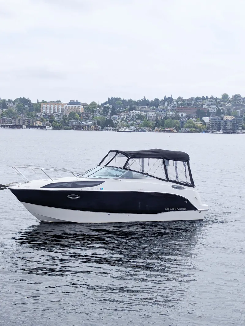 The Image of 2010 Bayliner 255 SB boat on a calm lake with cityscape background. - 0