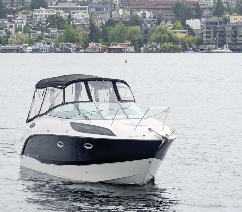 Slide: The Image of 2010 Bayliner 255 SB boat on a calm lake with cityscape background. - 2